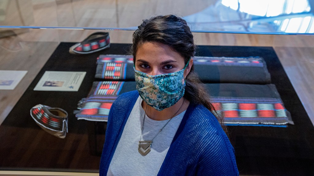 Woman in a fabric face mask in front of a display case featuring moccasins and leggings.