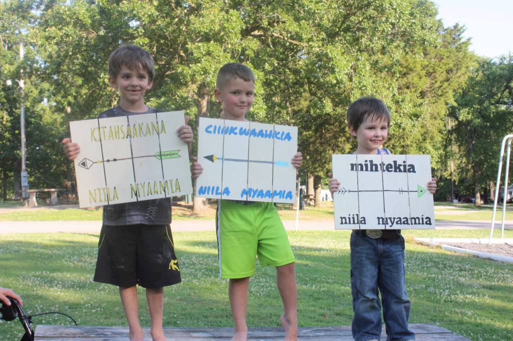 Three children holding white signs with their new Myaamia names.