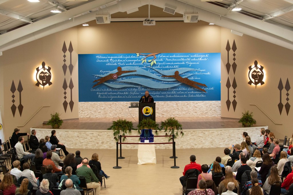 Akima Doug Lankford on stage speaking about the new decor of the expanded Miami Nation Council House.