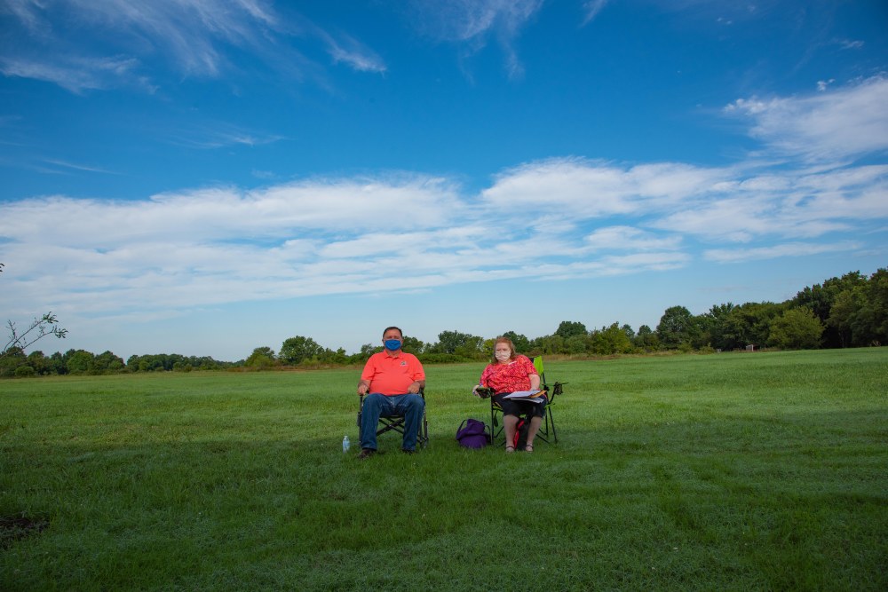 Two people wearing masks, sitting in lawn chairs in a large field.