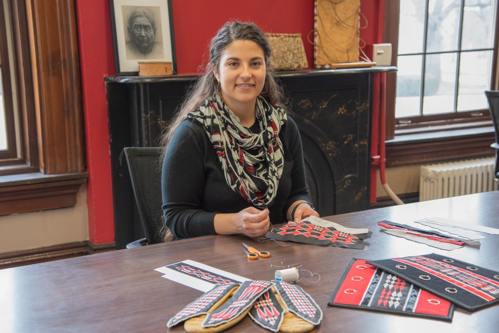 Kara Strass with several ribbonwork projects in front of her on the table.