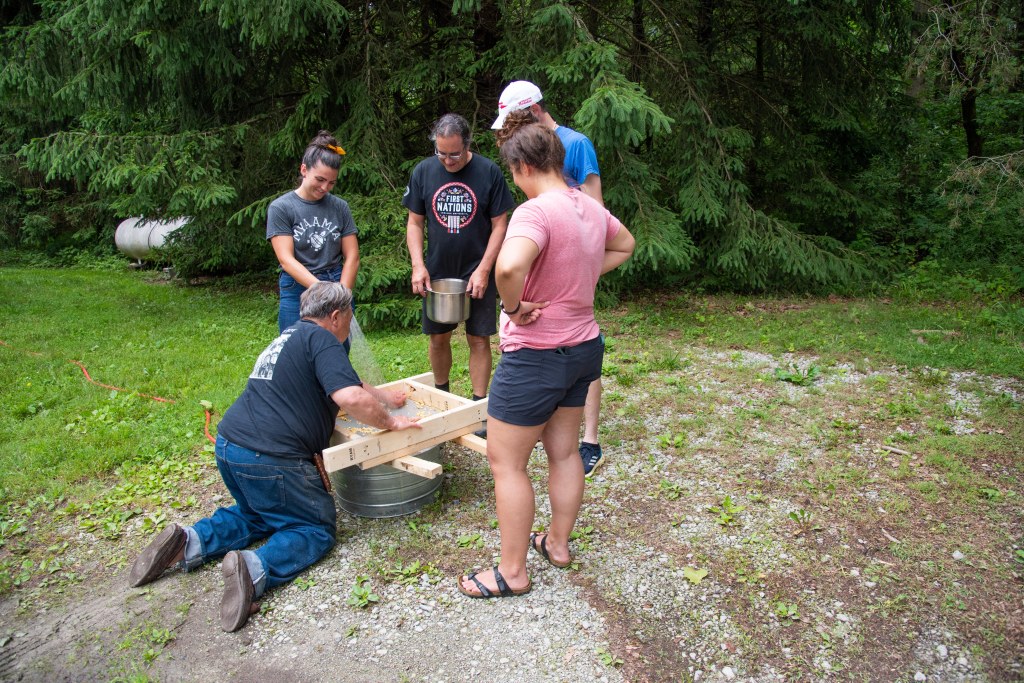 Myaamia citizens watching a man sifting corn.