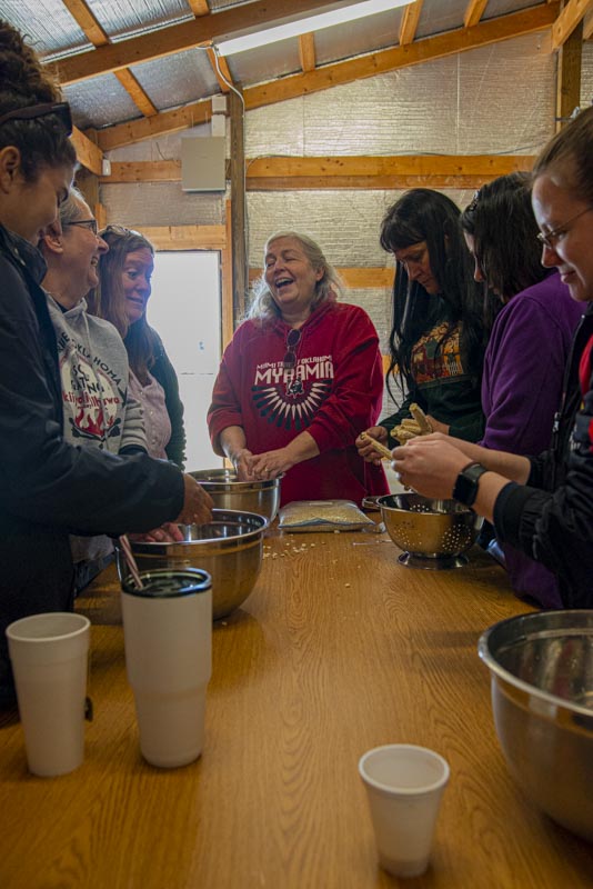 Women gathered around a table removing kernels of Myaamia corn from the cobs by hand
