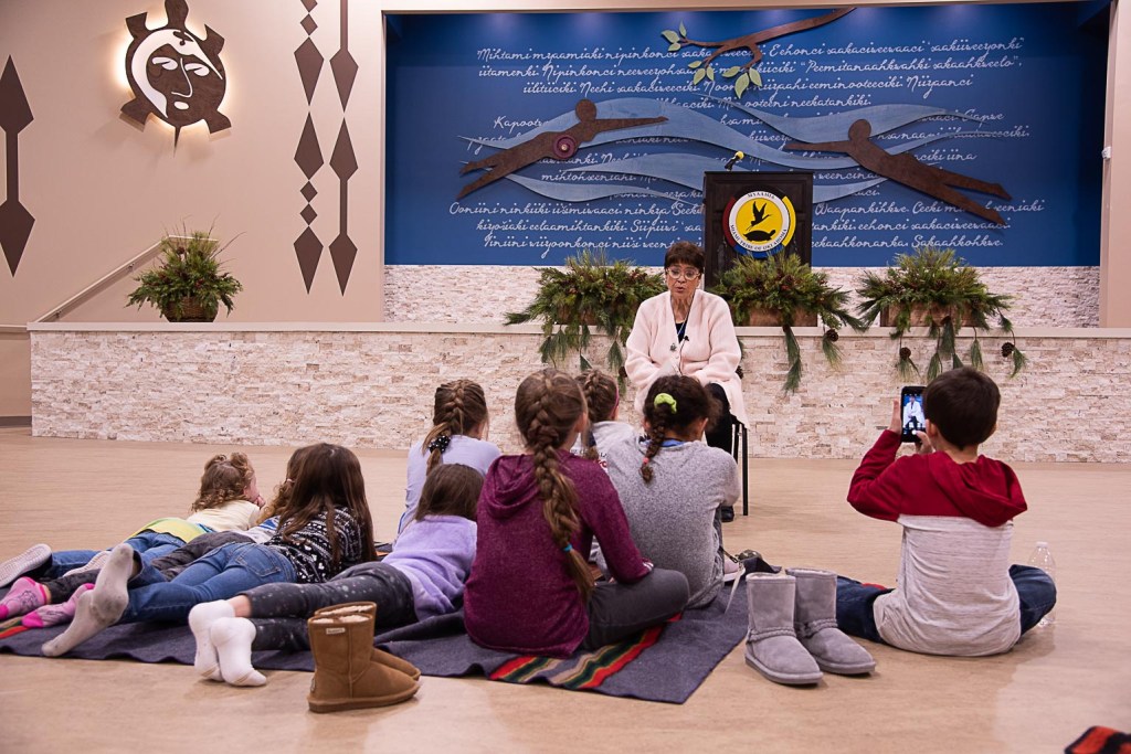 An elder woman sitting in front of a group of children telling a story