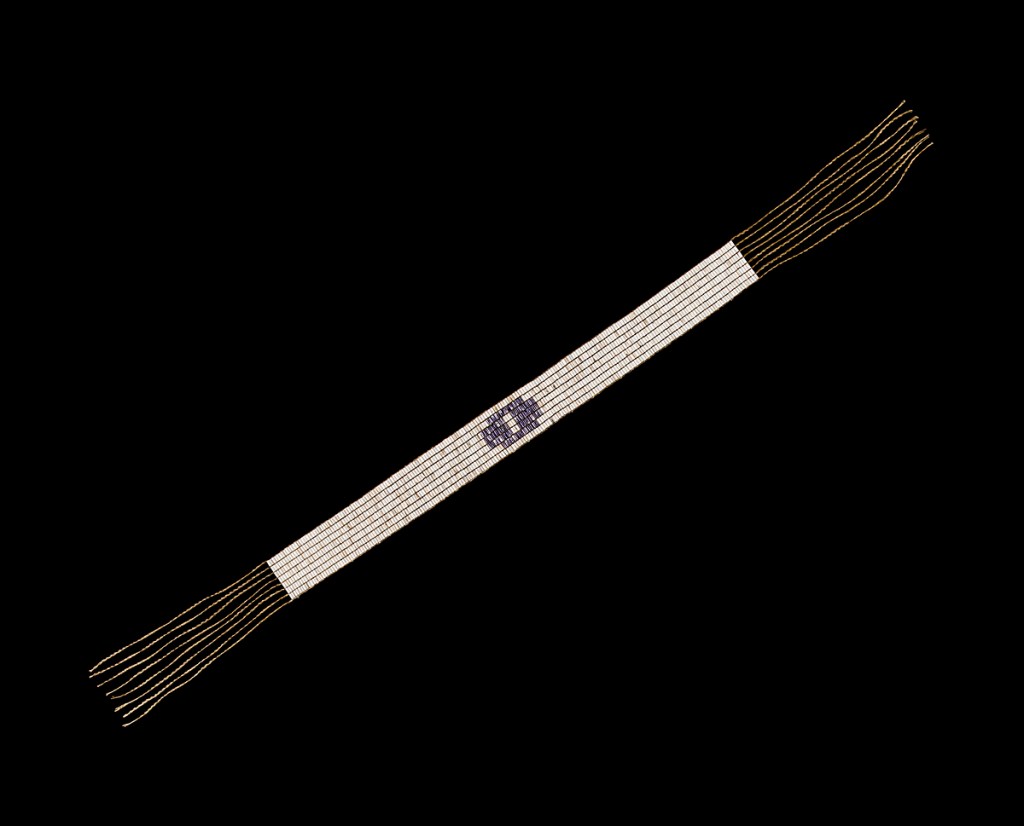 A picture of a white wampum belt with a purple symbol.