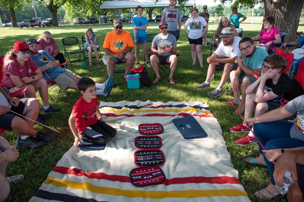 Group of people surrounding a blanket with moccasin game pieces.