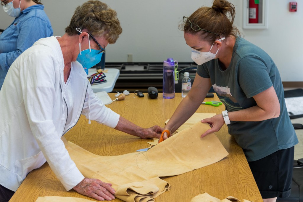 Two women working together to cut hide for moccasins.