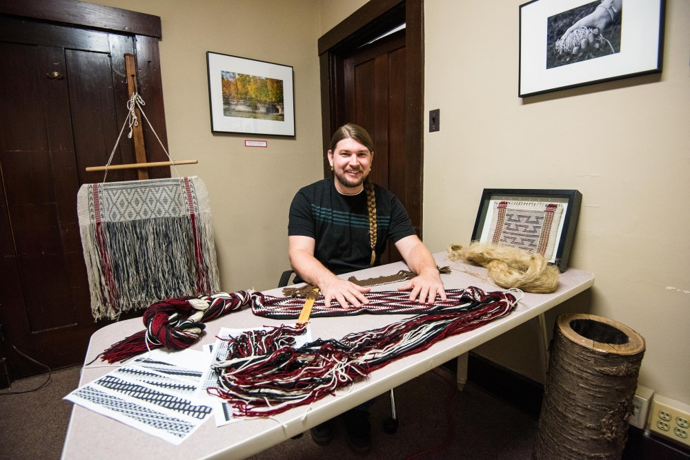 A man surrounded by several examples of his textile work