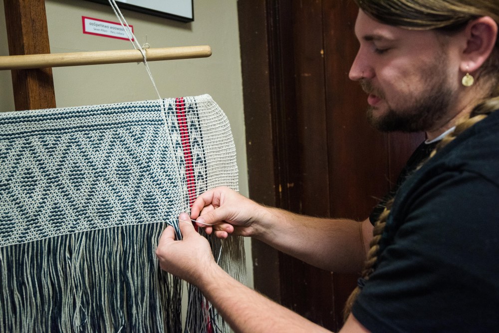 A man demonstrating a weaving technique on a bag