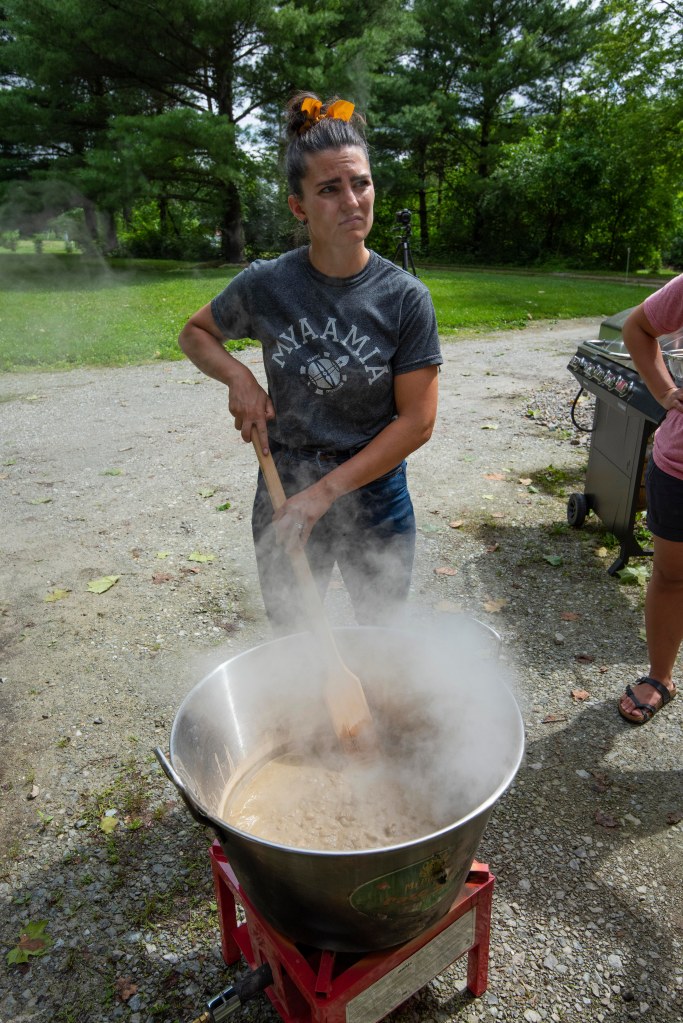 A woman using a large wooden spoon to stir a large pot