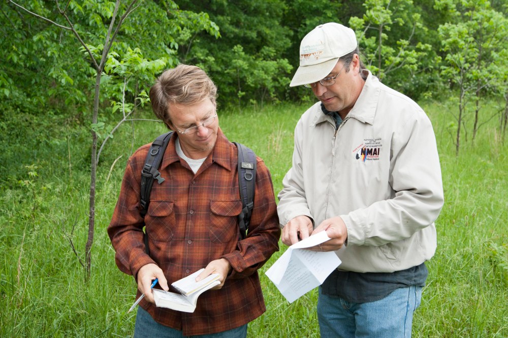 Two men consulting field notes in a large natural area