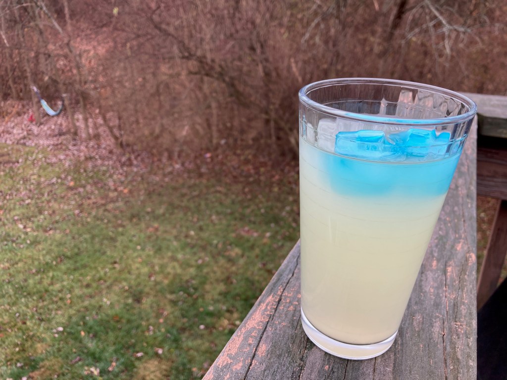 Glass of lemonade on a balcony railing overlooking a grassy area