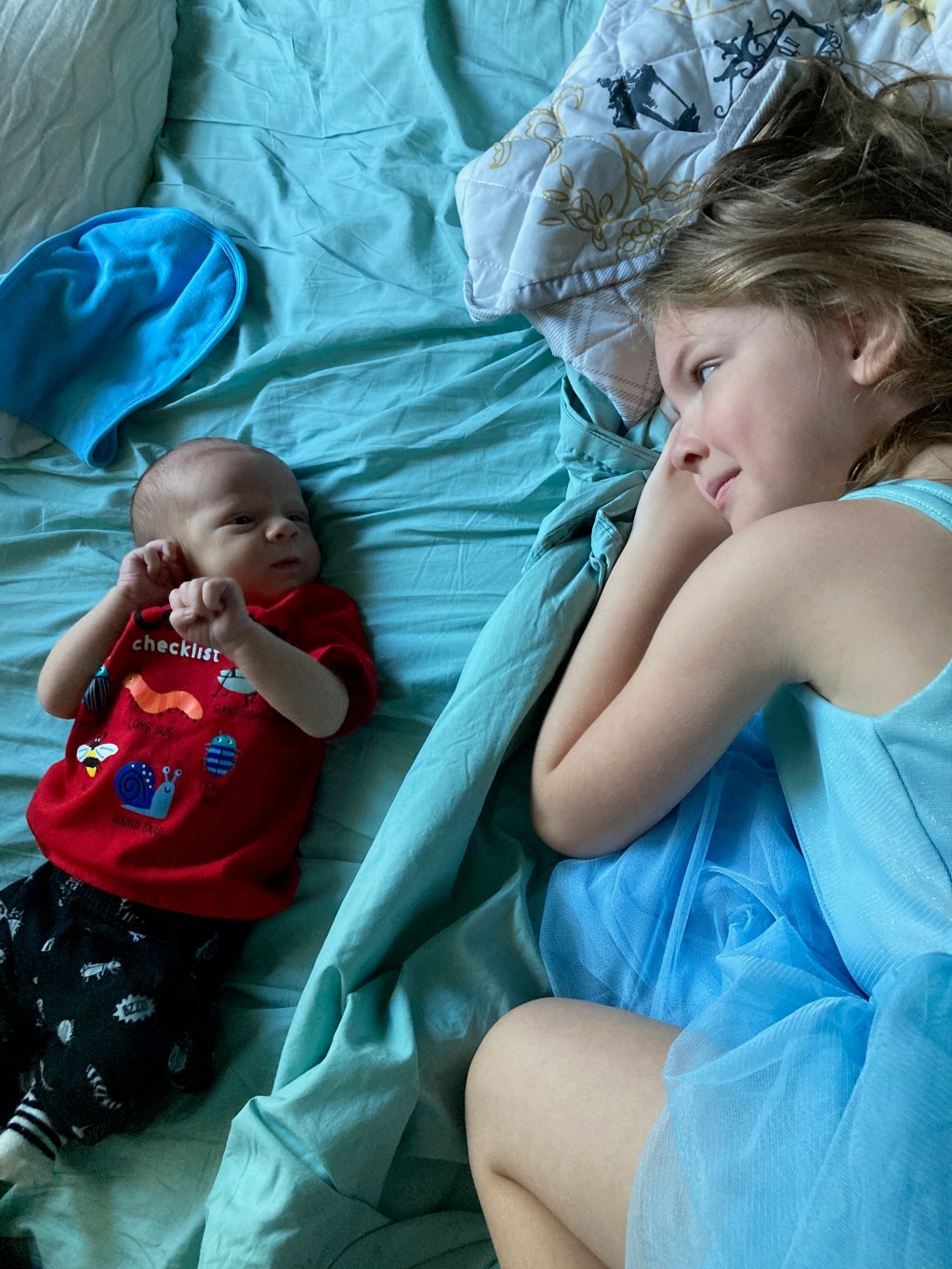 Girl laying next to and looking at a newborn