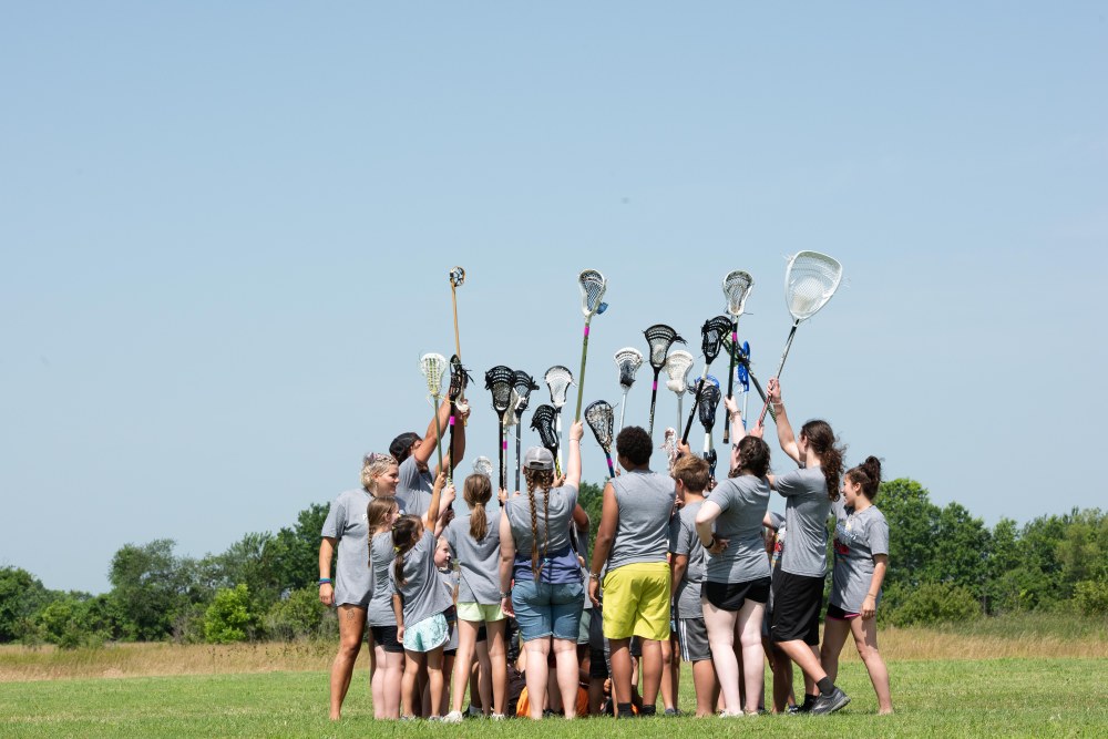 Group of people in a huddle with raised lacrosse sticks
