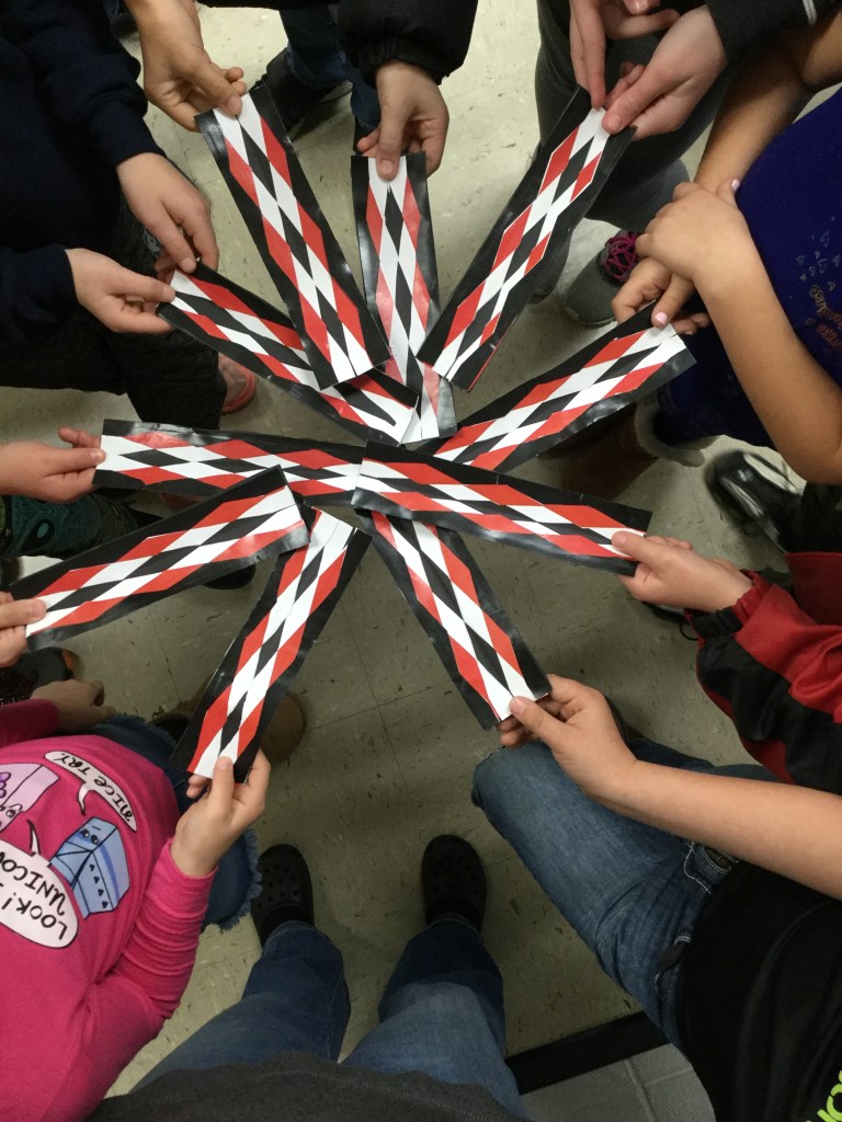 Students in a circle holding out completed ribbonwork inspired bookmarks