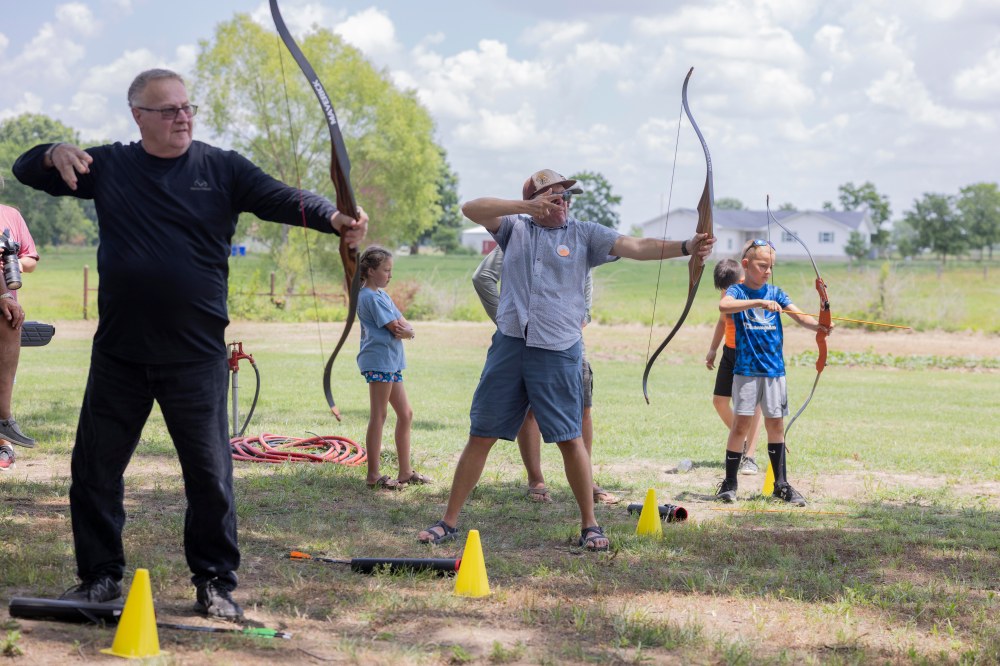 Two adults and a child shooting arrows at a target