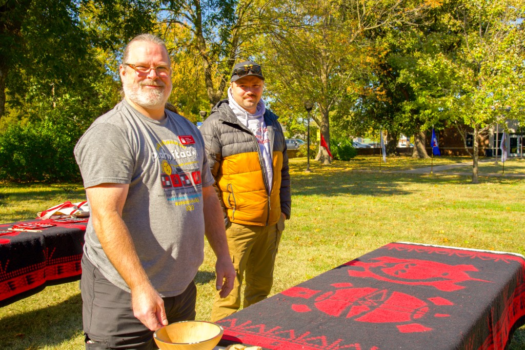 Two men smile for the camera as they set up a table covered by a blanket