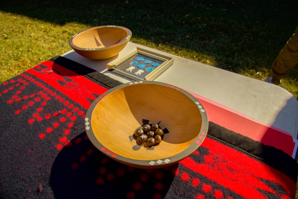 A table covered by a blanket with two wooden bowls containing 8 Kentucky Coffee Bean game pieces each set on top