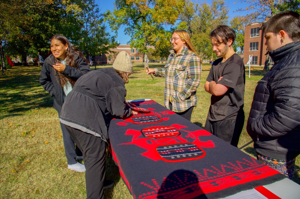A team of three watches as an opponent hides a game piece under a game pad