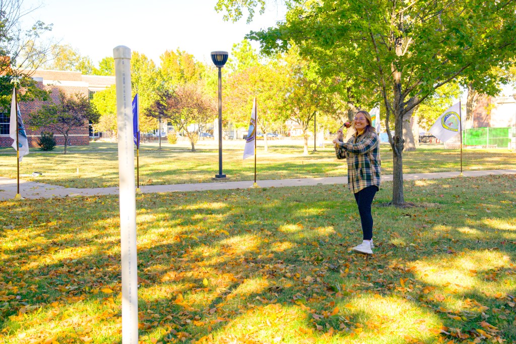 Woman with a lacrosse ball in the net of a wooden stick aims at a PVC goal post