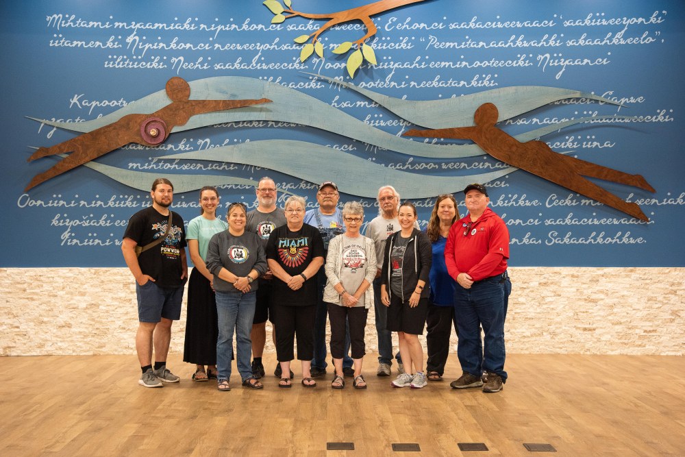 A group of about 10 people pose for a group photo in front of a mural at the Miami Tribe of Oklahoma's Council House