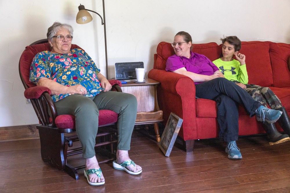 A woman sits in a rocking chair telling a story, a woman and young boy sit to right listening.