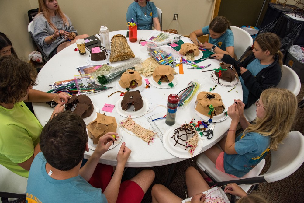 A group of 10 people sit around a table, each with a craft project in front of them.