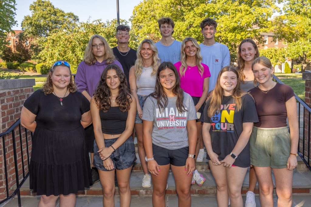 About 12 students stand outside on a summer evening, posing for group photo