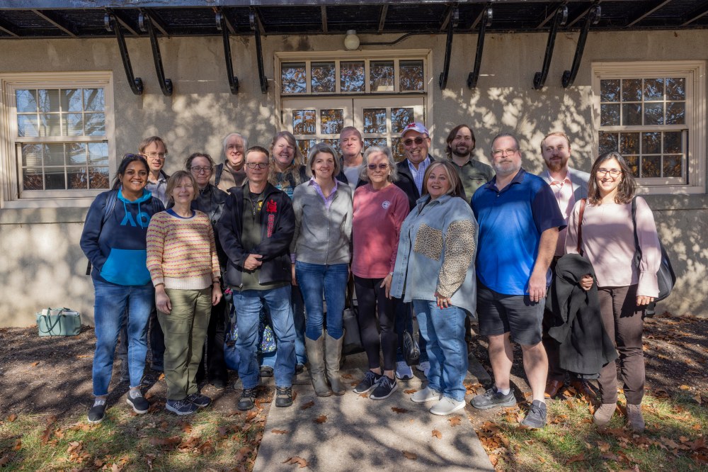 A group of about 15 people pose for a group photo outside.