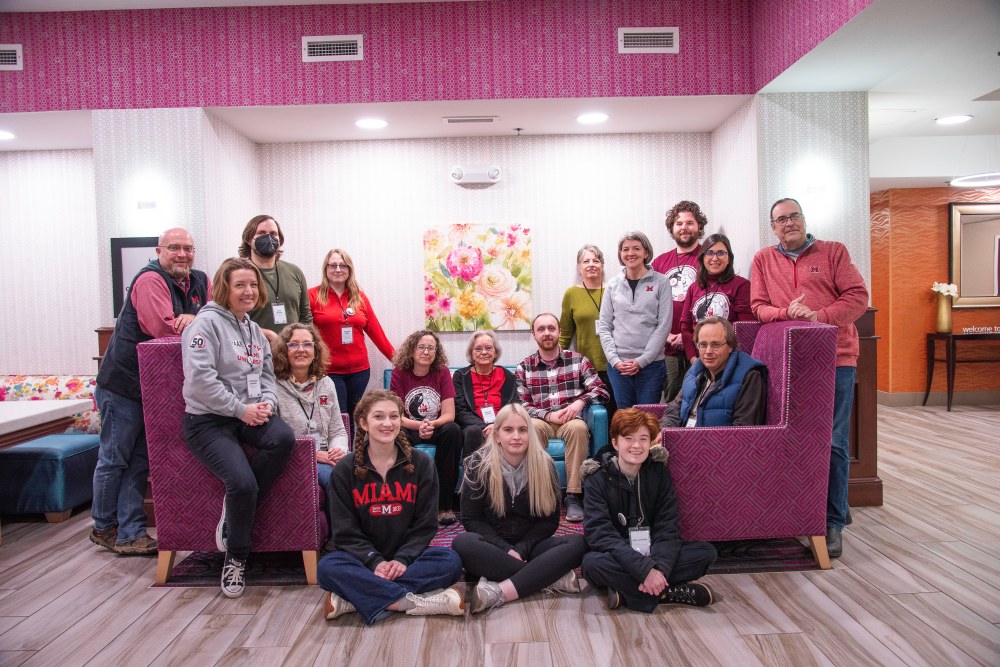 About 20 people pose together for a group photo in a hotel lobby