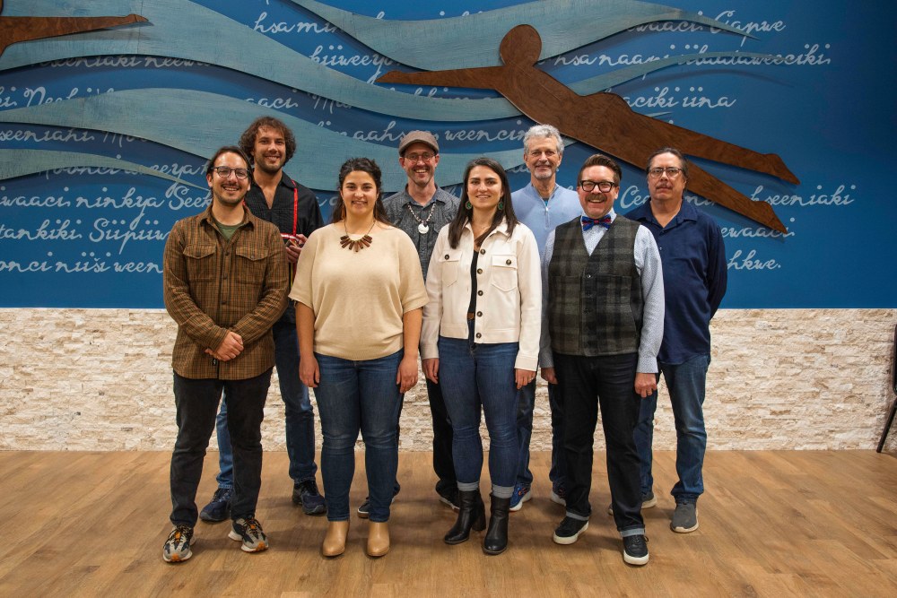 A group of 8 people stand on stage to pose for a photo.