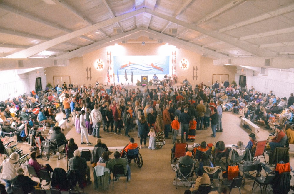 A large group of people form a spiral formation around a fake fire in the center of the room.