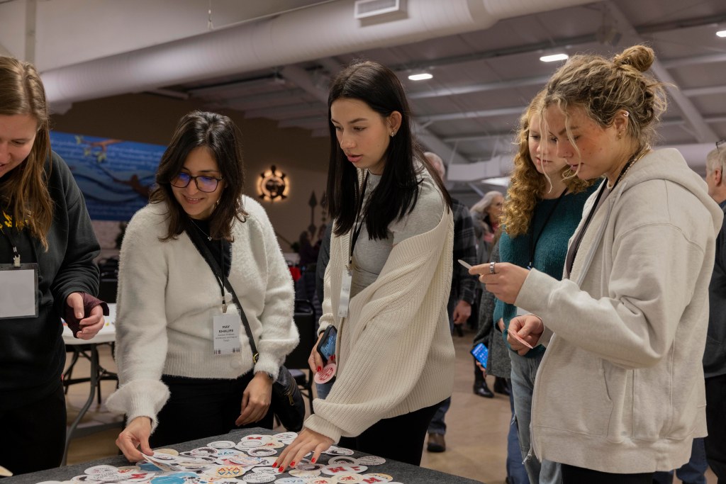 Four women stand around a table choosing a design for their pin