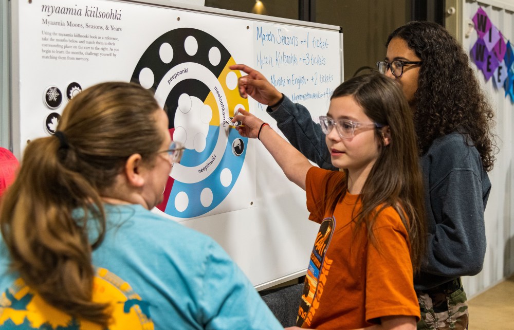 Two tribal youth try to place their game pieces in the correct spot on a board