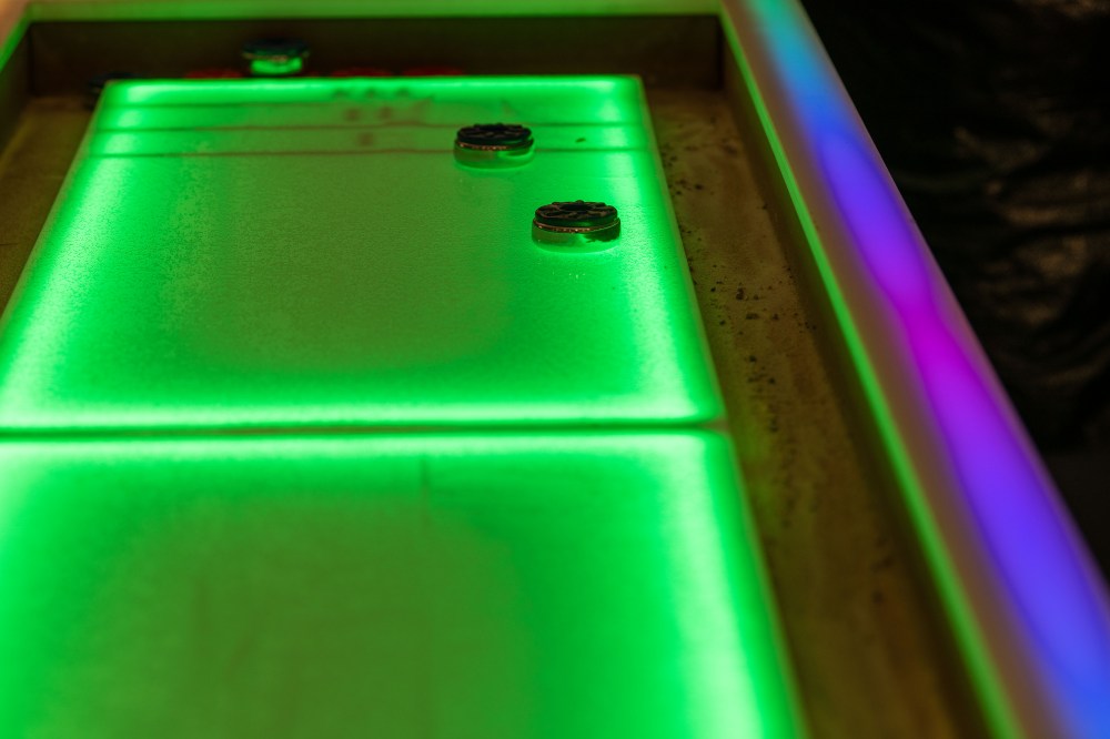 A shuffleboard board glows green from LED lights