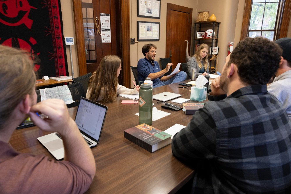 A group of people sit around a conference table listening to a man speak