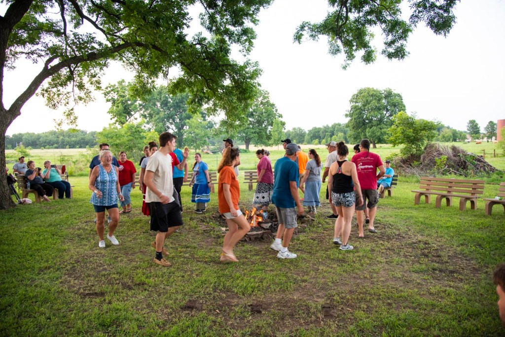 A group of people participate in a stomp dance outside at the Drake House