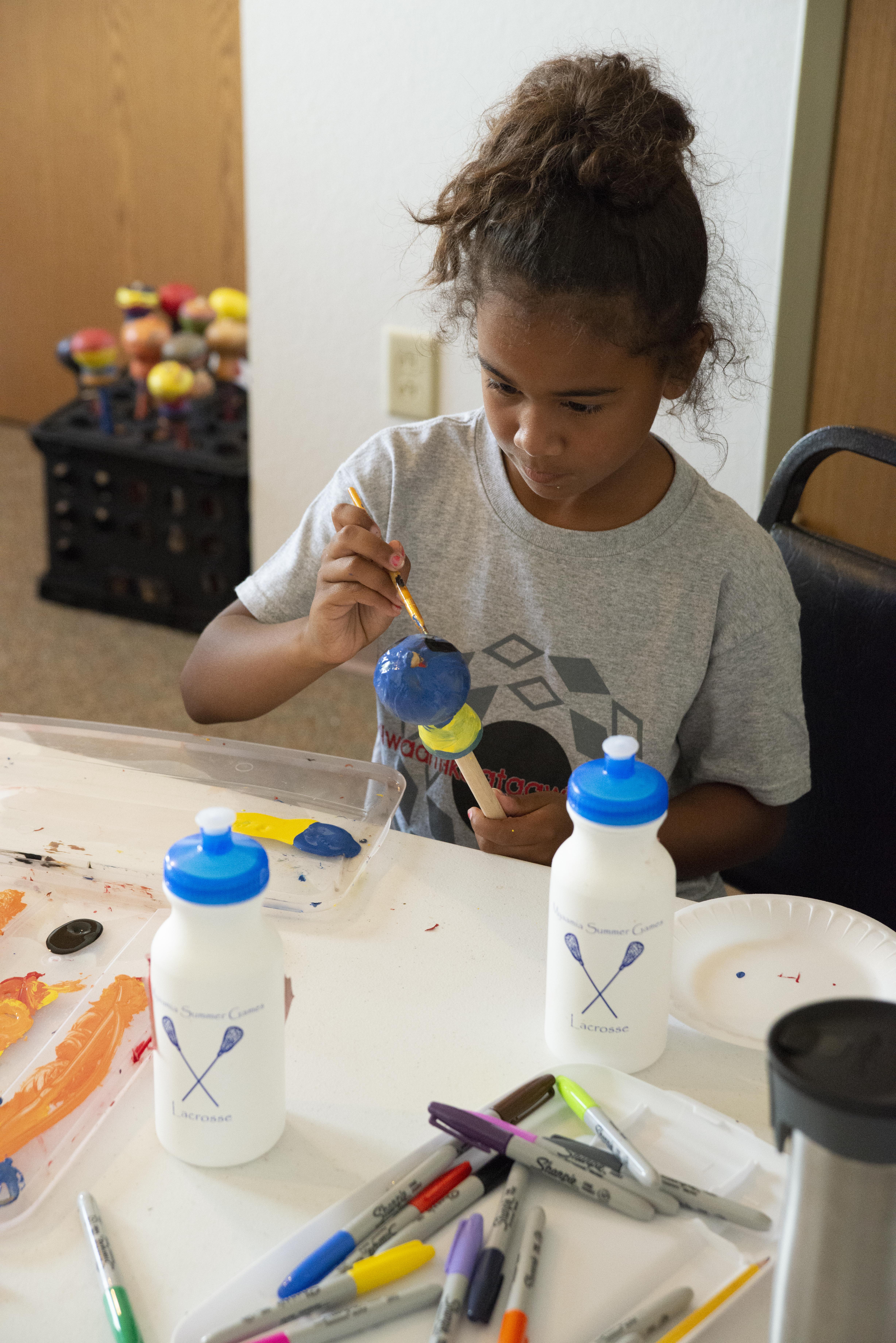 A young girl paints a gourd rattle