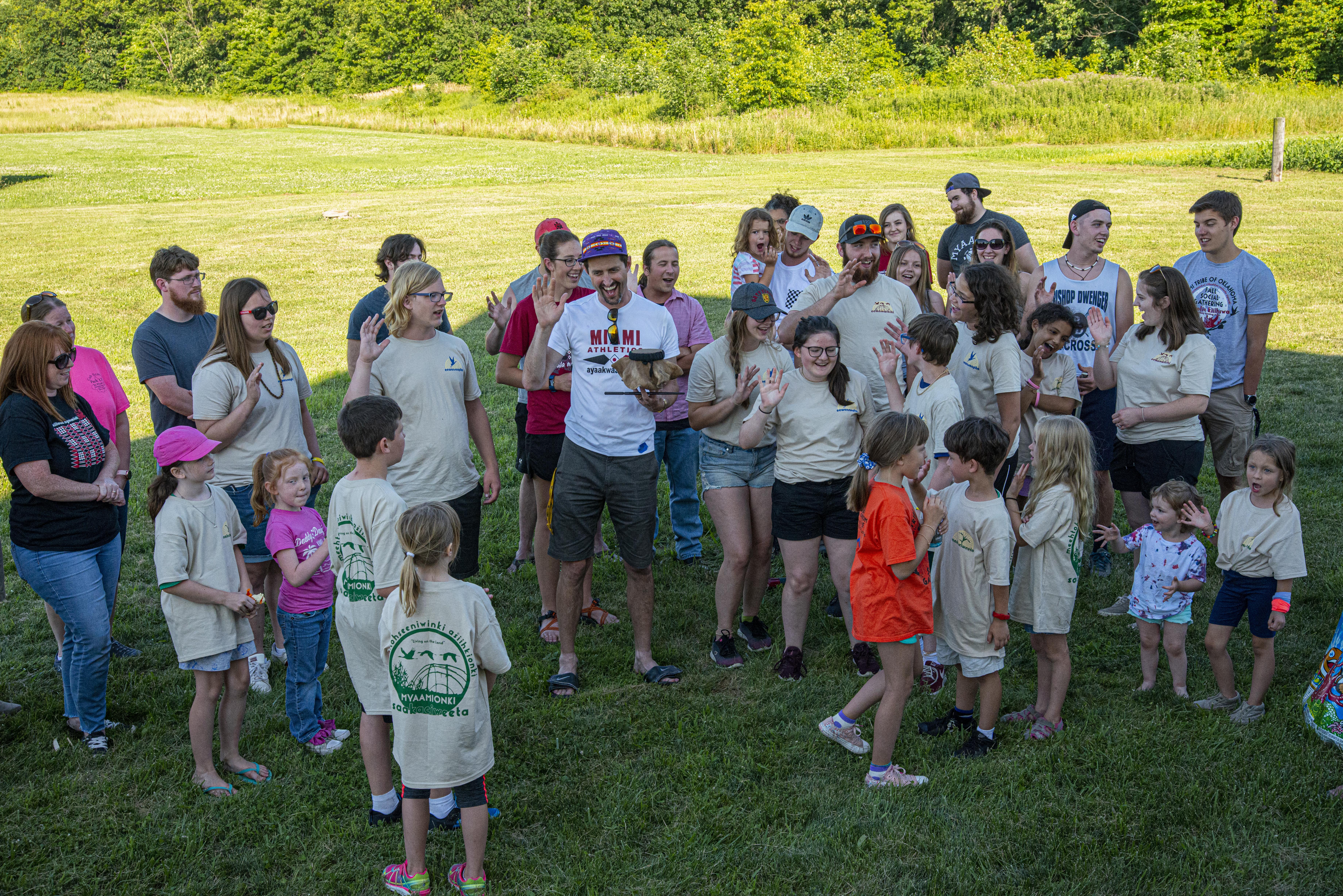 A group of children and adults stand in a group singing, dancing and laughing