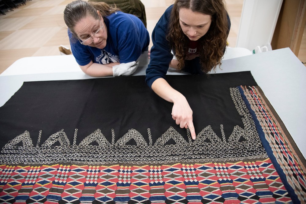 MHMA staff stand over a wrap skirt with ribbonwork