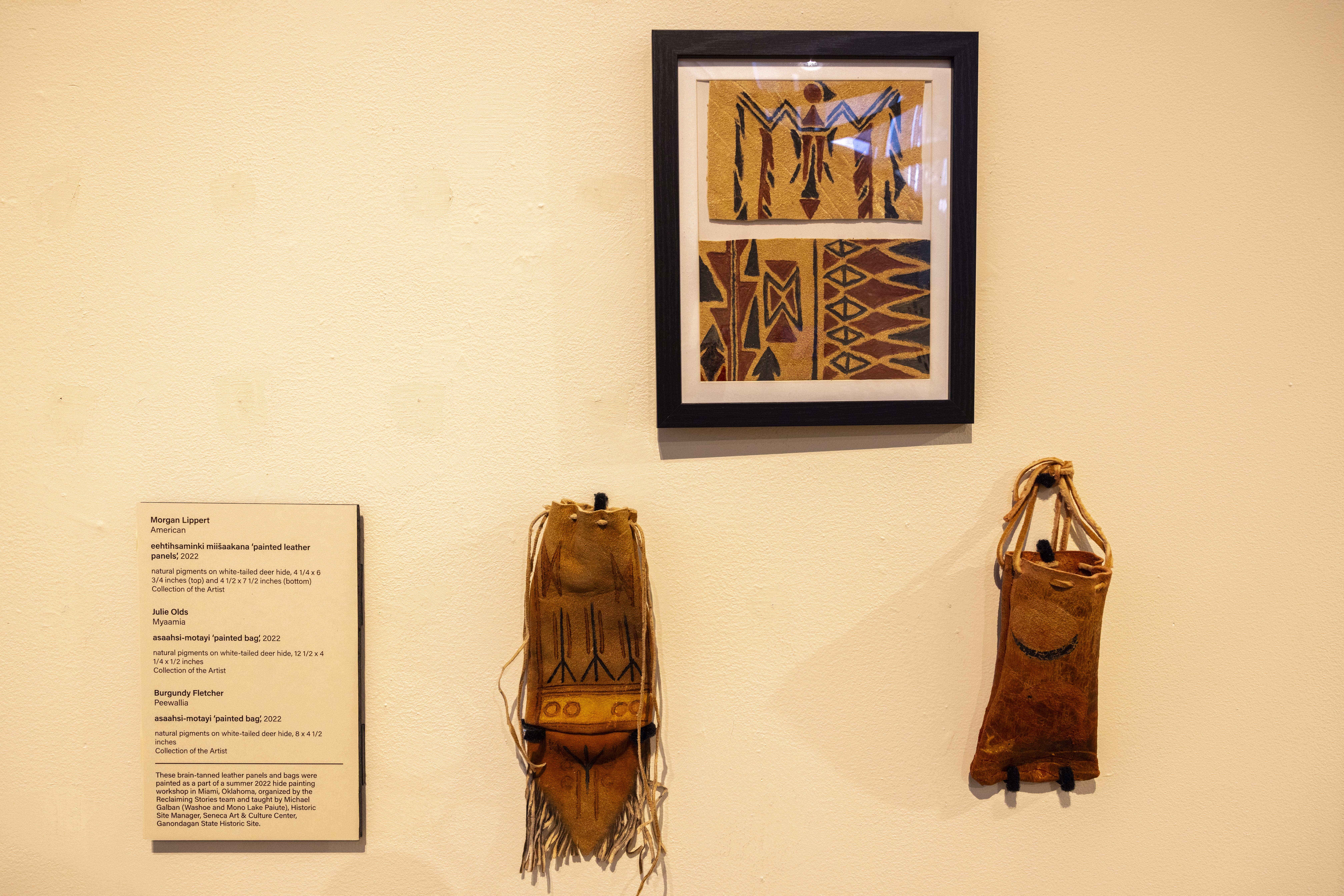 Framed painted hide pieces hanging above two painted hide bags