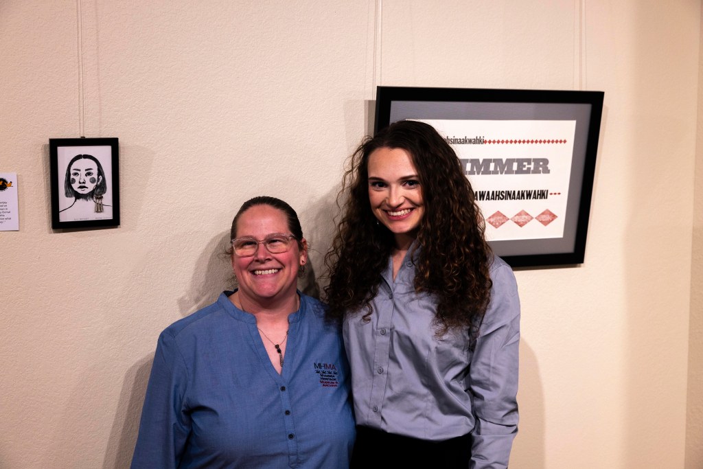 Two women stand in front of pieces of art at the Myaamia Heritage Museum and Archive.