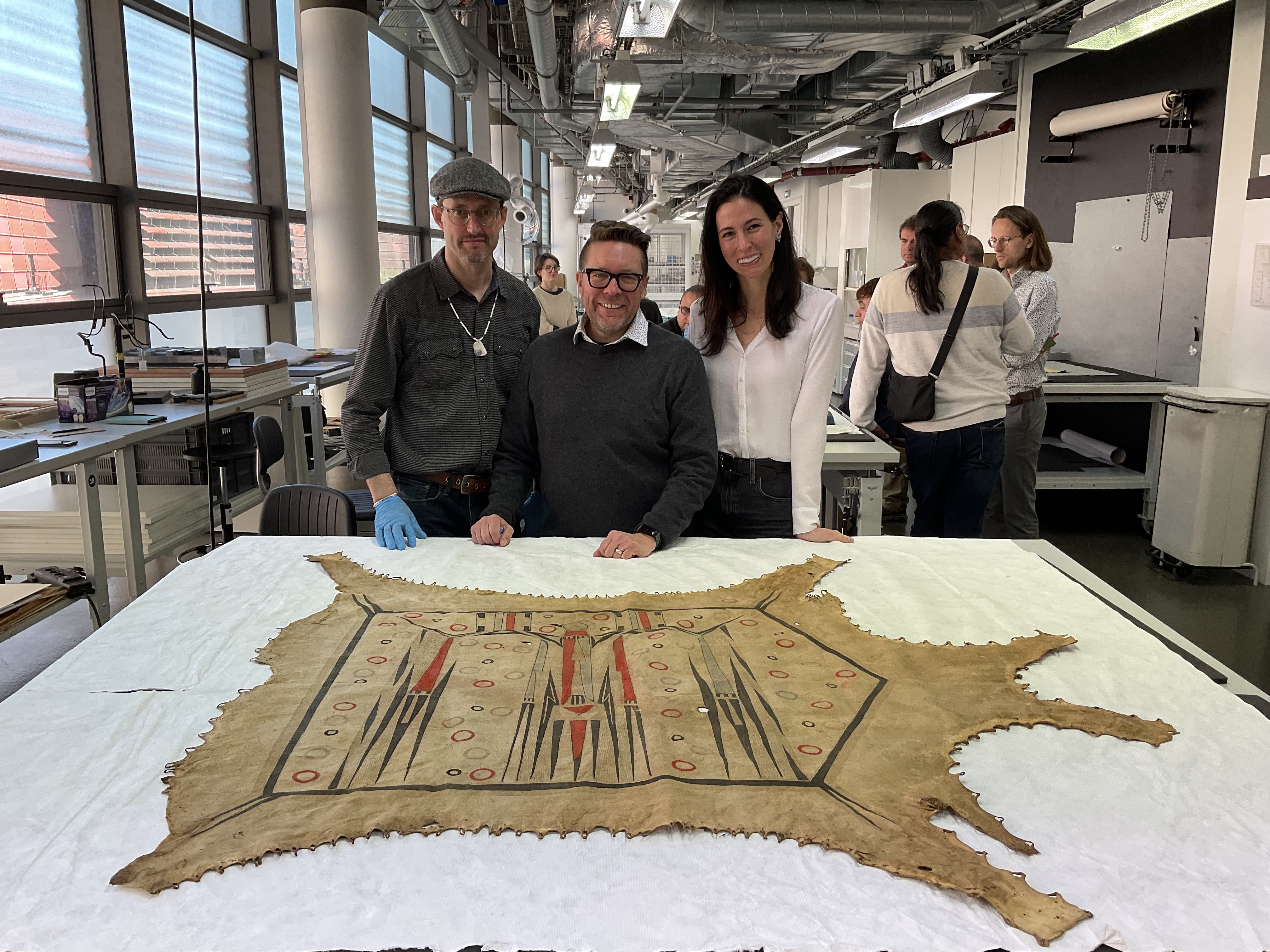 A group of people posing behind a table featuring a large painted hide robe