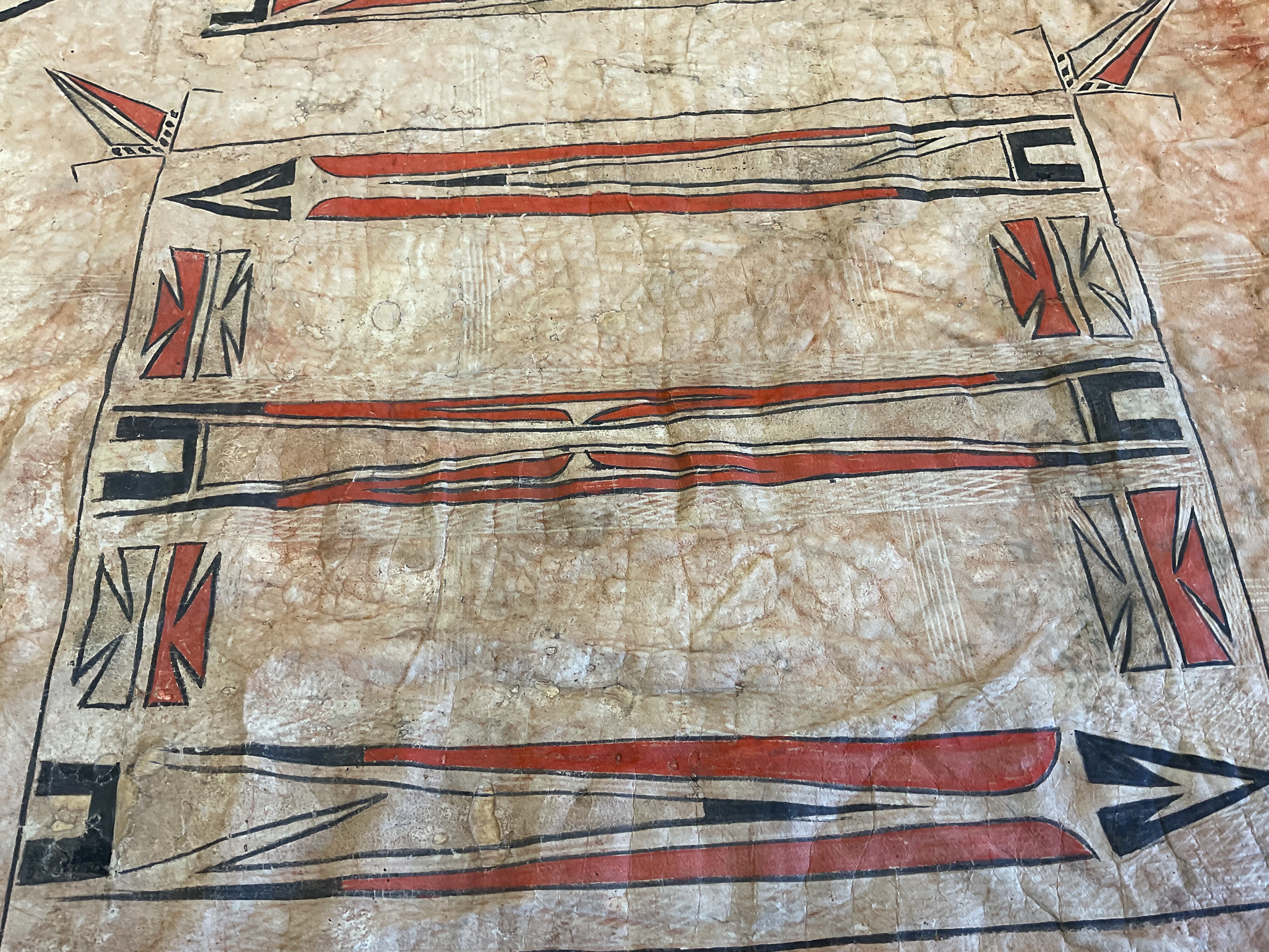A close up of a painted hide. The design features elongated triangles and hatch marks in clear, black, and red pigments.