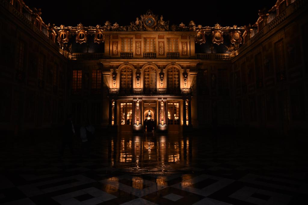 A building is partially lit in the darkness. The building lights are reflected in the puddles of the dark patio in front of the building.