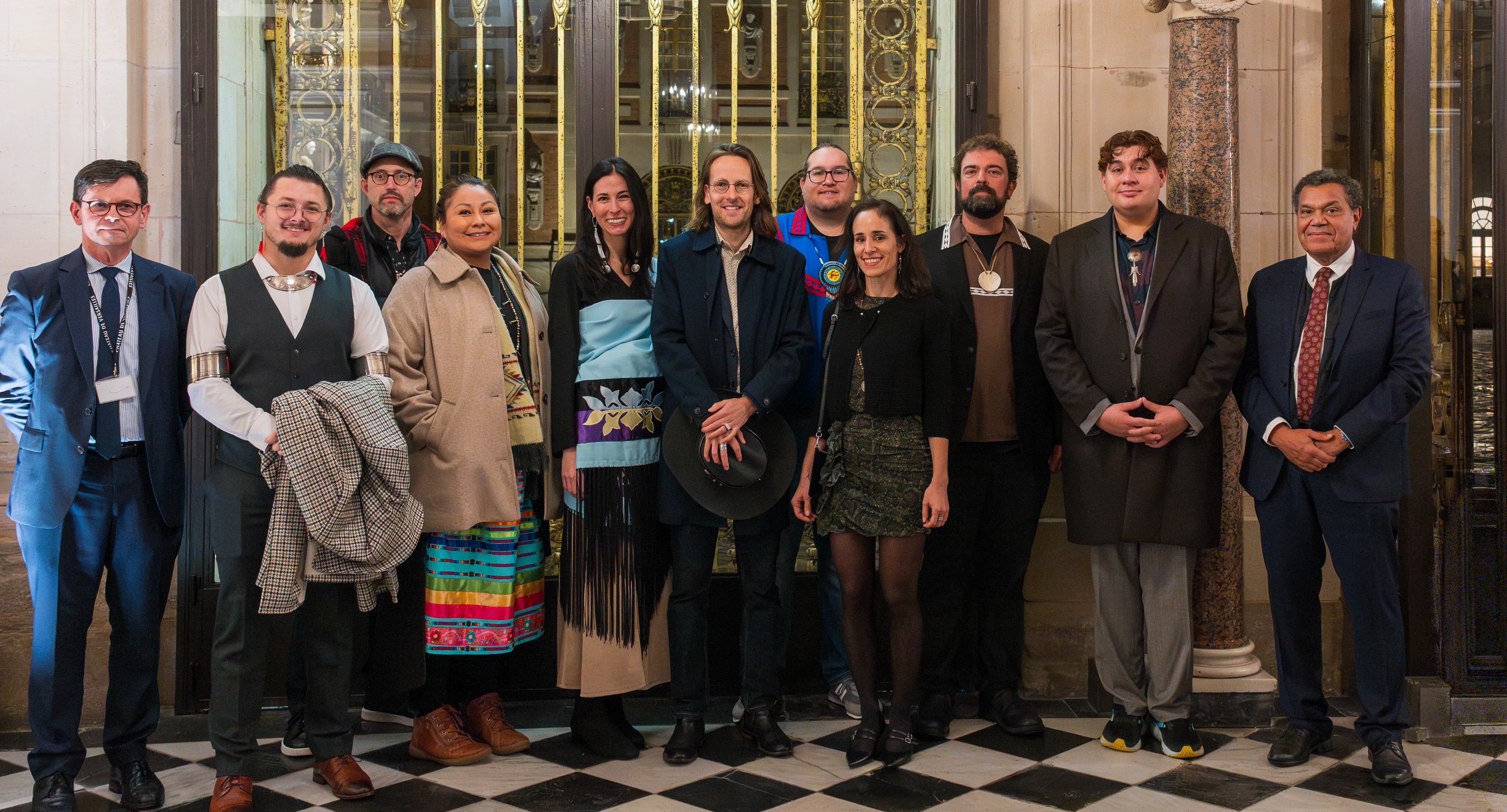 A group of 11 people stand in front of ornate doors.